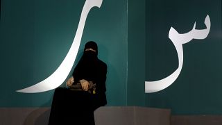 مرأة تجلس عند لافتة مكتوبة بحروف عربية خلال حدث ثقافي  حديقة الواجهة المائية بجدة/ المملكة العربية السعودية