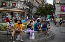 People wearing face masks to prevent the spread of coronavirus, sit on a bench street in downtown Madrid, Spain, Tuesday, July 28, 2020.