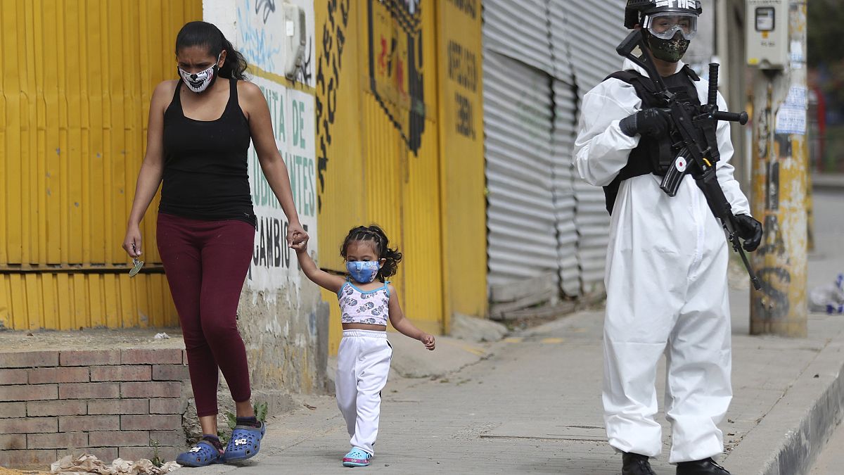Una mujer y una niña pasan junto a un militar con traje de protección en Bogotá, Colombia