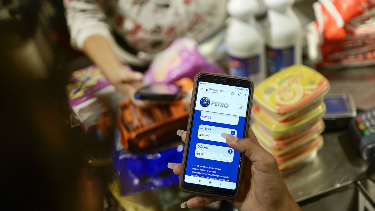 Una empleada muestra su teléfono móvil mientras calcula el monto de la compra en Petros en una tienda  donde se acepta la criptomoneda venezolana, en Caracas, Venezuela.