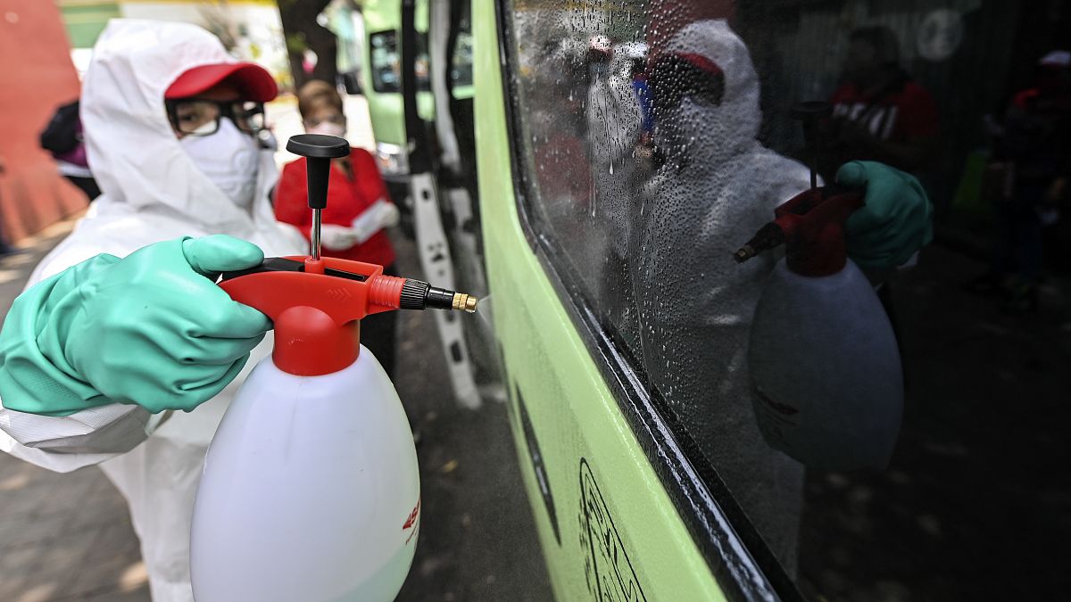 Un empleado con equipamiento de protección limpia un vehículo de transporte público en Ciudad de México
