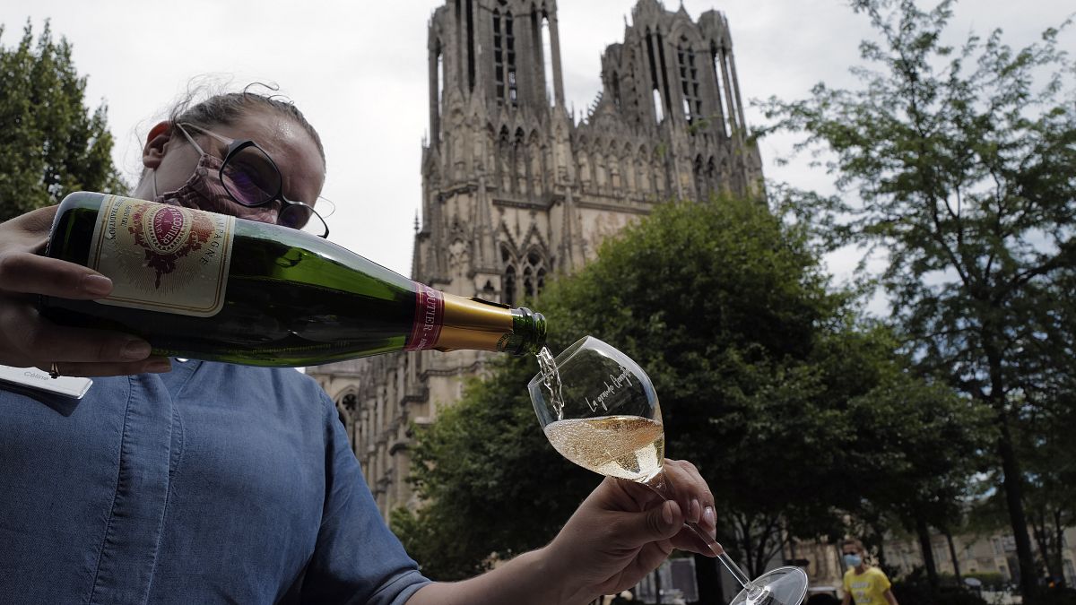 A waitress serves a glass of champagne at La Grande Georgette restaurant in front of the cathedral in Reims, onTJuly 28, 2020.