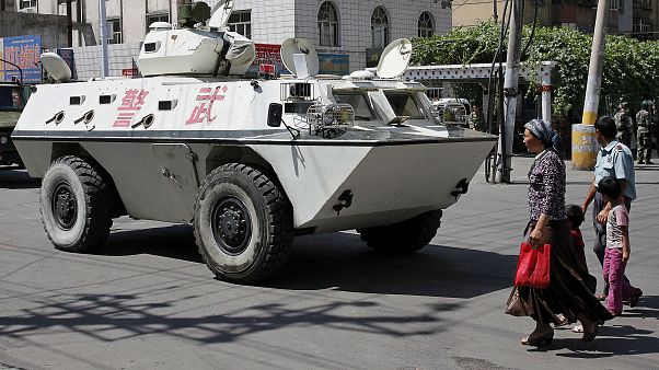 صينيون من الإيغور يمشون بالقرب من مدرعة صينية صينيون من الإيغور يمشون بالقرب من مدرعة صينية