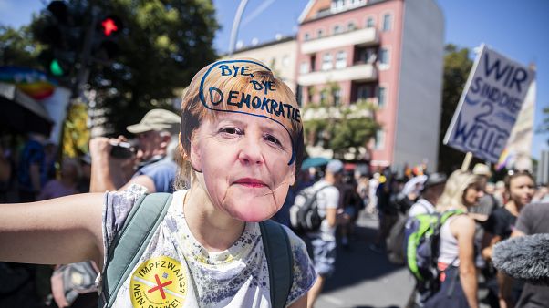 Una mujer lleva una máscara de Angela Merkel con la inscripción "adíos democracia" en la manifestación contra las restricciones en Berlín, Alemania, el 1 de agosto, 2020. Una mujer lleva una máscara de Angela Merkel con la inscripción "adíos democracia" en la manifestación contra las restricciones en Berlín, Alemania, el 1 de agosto, 2020.