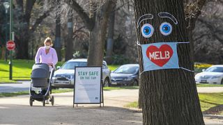 A woman pushes a pram past a large face mask pinned to a tree in Melbourne on August 3, 2020 after the state announced new restrictions as the city battles fresh outbreaks.