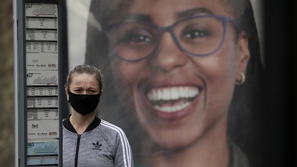 Una mujer con mascarilla espera junto a una parada de autobús en el Reino Unido Una mujer con mascarilla espera junto a una parada de autobús en el Reino Unido