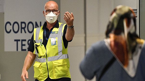 Duesseldorf Havaalanı'na gelen yolcuları, Covid-19 test merkezine yönlendiren bir görevli Duesseldorf Havaalanı'na gelen yolcuları, Covid-19 test merkezine yönlendiren bir görevli