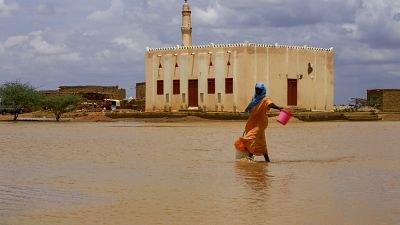 A Sudanese woman crosses a flooded area, as a result of flooding and torrential rain, in the town of Osaylat.