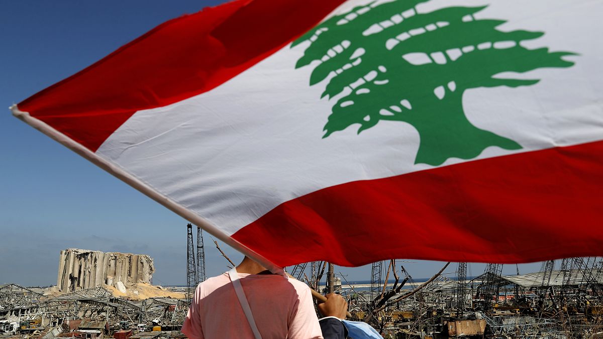 مردی با در دست داشتن پرچم لبنان به ویرانه‌های ناشی از ��نفجار بیروت می‌نگرد
