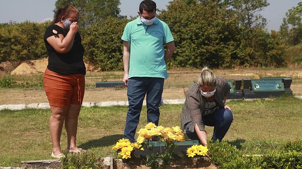 Sisters Valeria Melo da Silva, left, and Viviane, her husband Luigi do Nascimento visit the grave of their mother who died of COVID-19 at a cemetary in Brazil. Sisters Valeria Melo da Silva, left, and Viviane, her husband Luigi do Nascimento visit the grave of their mother who died of COVID-19 at a cemetary in Brazil.