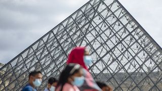 A family wearing face masks walk past the Louvre Museum in Paris on Saturday