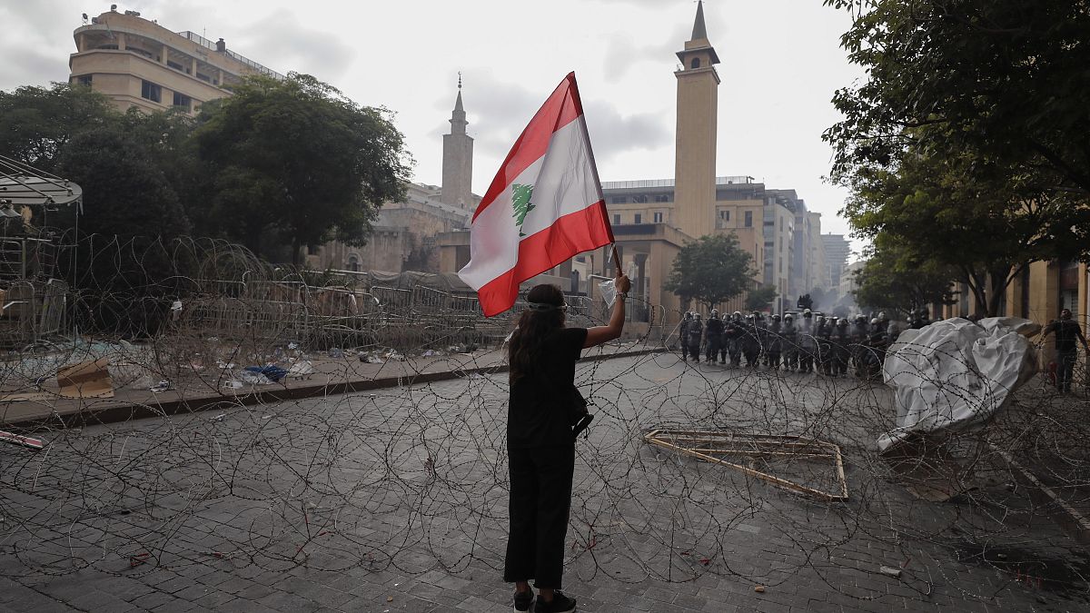 Egy nő libanoni zászlót lenget szemben a rendőrsorfallal