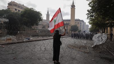 Egy nő libanoni zászlót lenget szemben a rendőrsorfallal