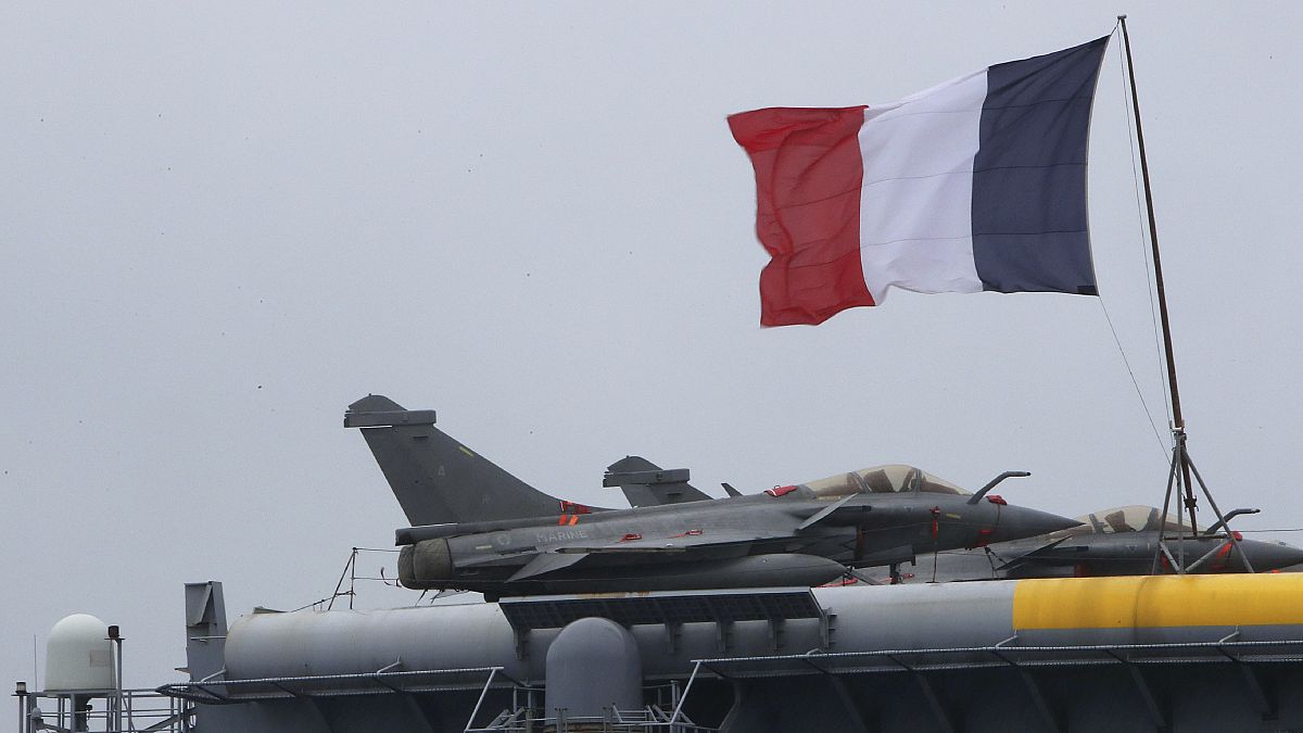 العلم الفرنسي يرفرف بالقرب من طائرات رافال الحربية علت حاملة الطائرات شارل ديغول التي رست في ميناء ليماسول الرئيسي بقبرص