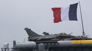 العلم الفرنسي يرفرف بالقرب من طائرات رافال الحربية علت حاملة الطائرات شارل ديغول التي رست في ميناء ليماسول الرئيسي بقبرص