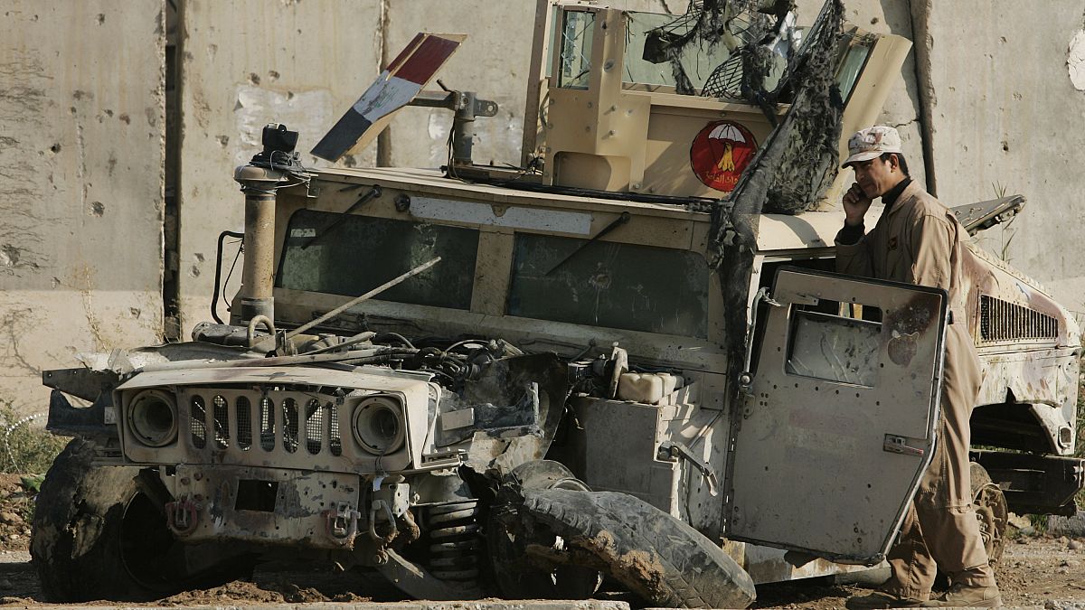 An Iraqi army soldier talks on his phone as he stands next to an army vehicle damaged in previous fighting, at an Iraqi army base in Sukor neighborhood