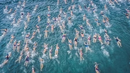 A crowd of wild swimmers in multicoloured caps take to the sea.