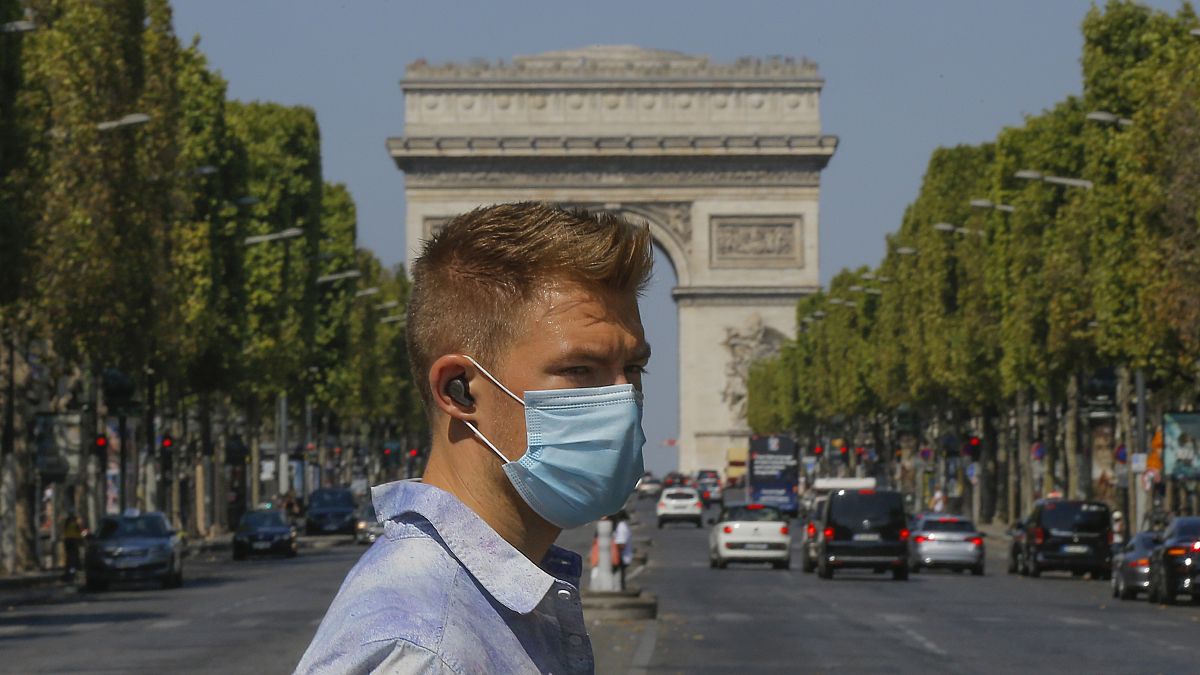 A man wearing a masks to prevent the spread of COVID-19 crosses the Champs Elysees avenue in Paris, Sunday, Aug 9, 2020.
