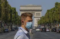 A man wearing a masks to prevent the spread of COVID-19 crosses the Champs Elysees avenue in Paris, Sunday, Aug 9, 2020.