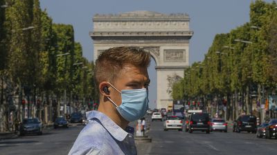 A man wearing a masks to prevent the spread of COVID-19 crosses the Champs Elysees avenue in Paris, Sunday, Aug 9, 2020.