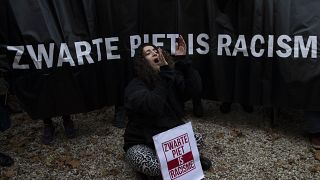 A Kick Out Zwarte Piet demonstrator sits in front of a banner during protests in The Hague in 2019.