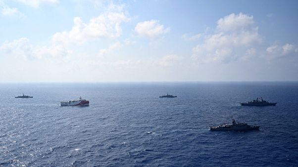 In this photo provided by the Turkish Defense Ministry, Turkey's research vessel, Oruc Reis, in red and white, is surrounded by Turkish navy vessel In this photo provided by the Turkish Defense Ministry, Turkey's research vessel, Oruc Reis, in red and white, is surrounded by Turkish navy vessel
