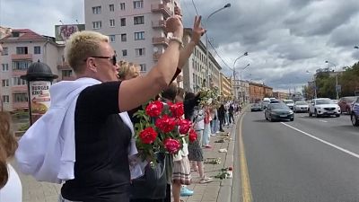 Women carrying flowers, standing on side of road in protest