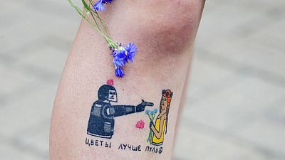 Tetoválás egy tüntetőn. A felirat nagyjából azt jelenti, hogy a virágok jobbak a töltényeknél