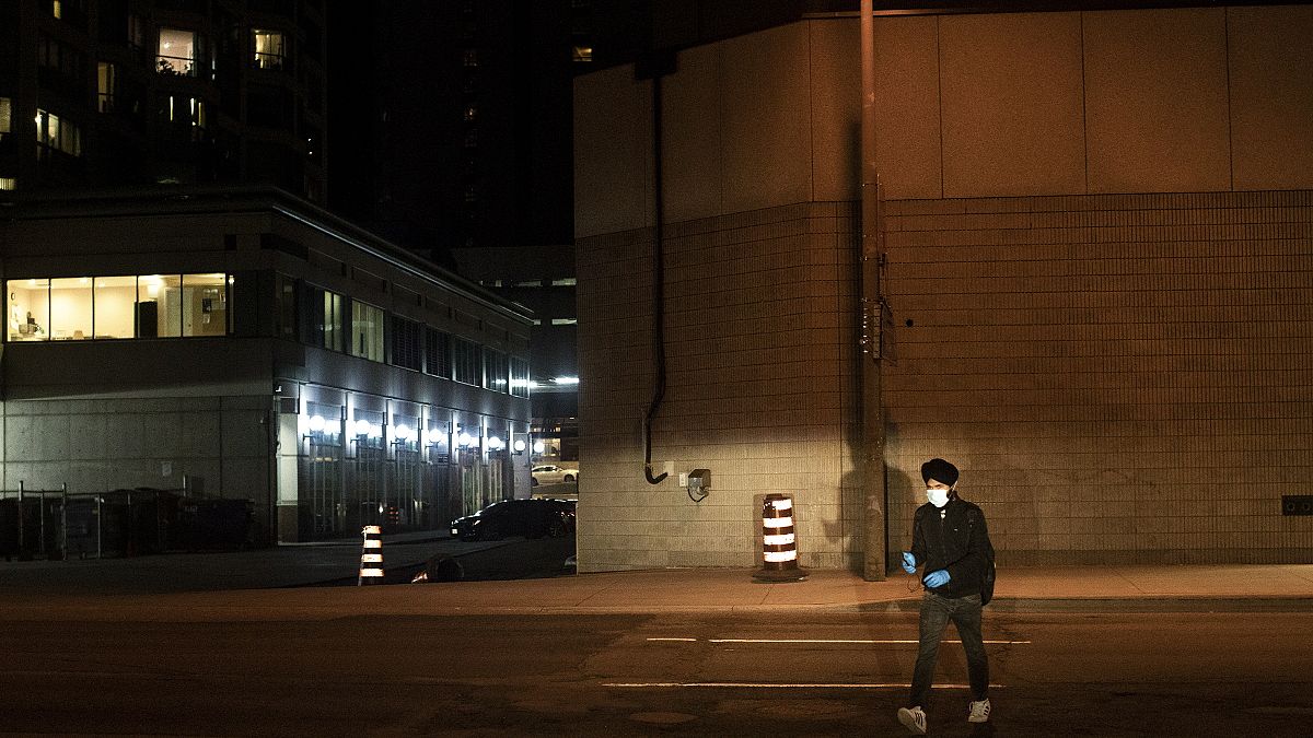 A man wearing protective gloves and a face mask as he crosses a road in Toronto, Ontario, Saturday, May 9, 2020, during the coronavirus pandemic.