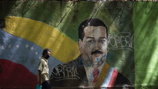 Un hombre camina junto al rostro de Nicolás Maduro pintado en un muro de Caracas
