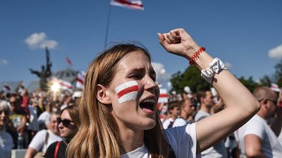 A woman Belarus opposition supporter with a drawing of a former white-red-white flag of Belarus used in opposition to the government punches the air.