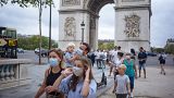 A family wearing protective face masks walk along on the Champs Elysee avenue, with Arc de Triomphe in background, in Paris, Saturday, Aug. 15, 2020.