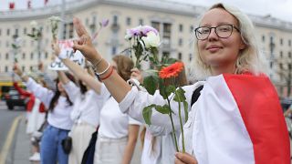 Belarusians protesting against disputed presidential elections results hold flowers and flash victory signs during a protest in Victory Square in Minsk, Belarus. August 20