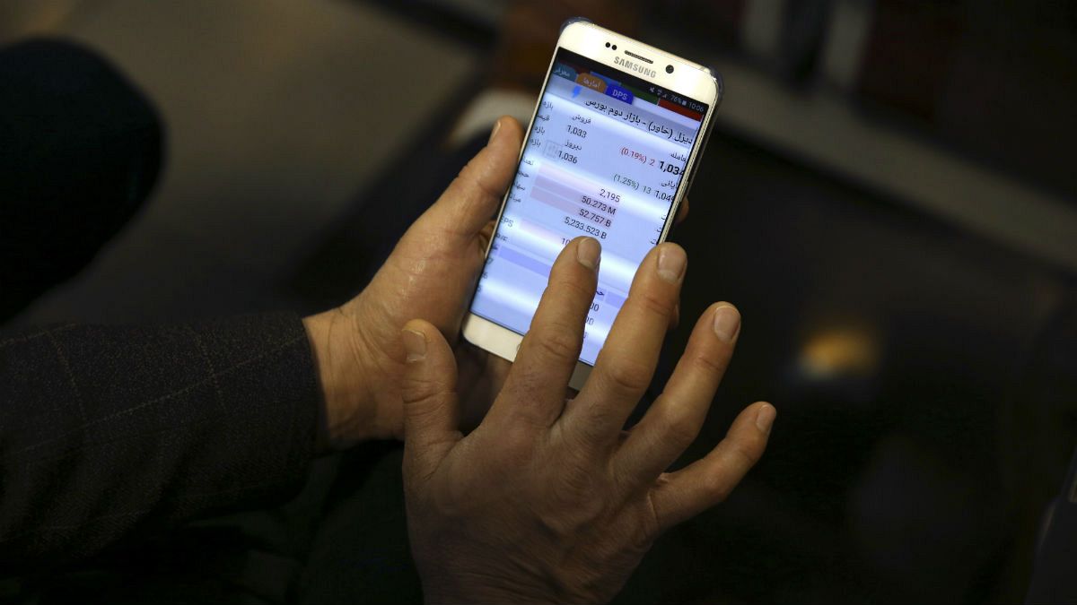An Iranian shareholder monitors stock prices on his mobile phone at the Tehran Stock Exchange in Tehran, Iran