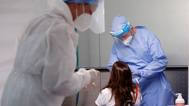 FILE - In this Aug. 20, 2020 file photo medical workers wearing protective gear collect swabs from a passenger arriving from one of four Mediterranean countries. FILE - In this Aug. 20, 2020 file photo medical workers wearing protective gear collect swabs from a passenger arriving from one of four Mediterranean countries.