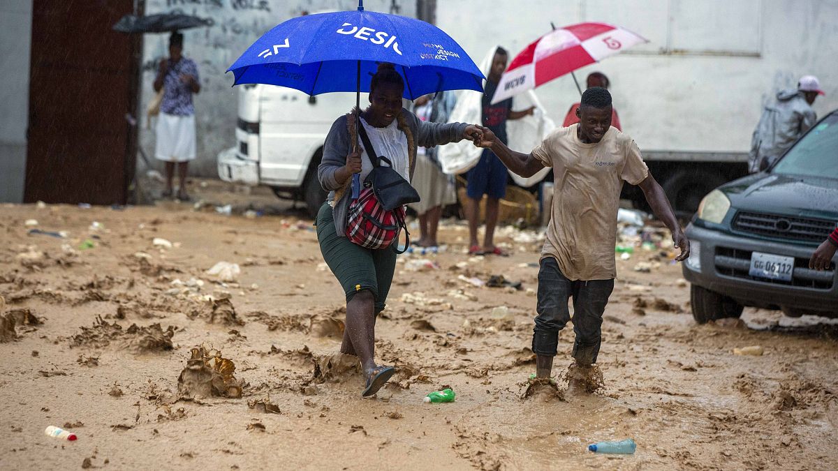 A woman is helped by a man to cross a flooded street during the passing of Tropical Storm Laura in Port-au-Prince, Haiti, Sunday, Aug. 23, 2020.