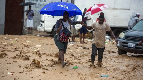 A woman is helped by a man to cross a flooded street during the passing of Tropical Storm Laura in Port-au-Prince, Haiti, Sunday, Aug. 23, 2020. A woman is helped by a man to cross a flooded street during the passing of Tropical Storm Laura in Port-au-Prince, Haiti, Sunday, Aug. 23, 2020.
