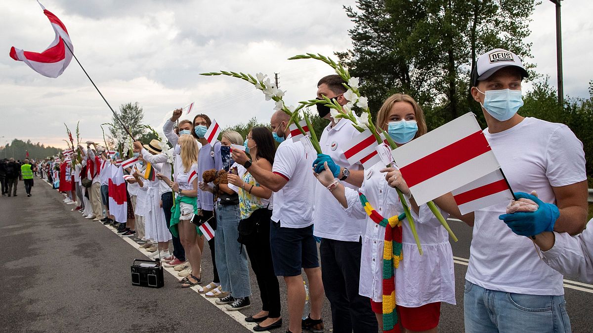 People hold hands, historical white-red-white flags of Belarus and flowers as they participate in a "Freedom Way"