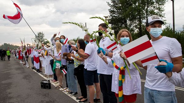 People hold hands, historical white-red-white flags of Belarus and flowers as they participate in a "Freedom Way" People hold hands, historical white-red-white flags of Belarus and flowers as they participate in a "Freedom Way"