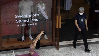 Egy pekingi sportboltból maszkban lép ki egy férfi, miközben maszk nélkül jógázik a bejáratnál egy nő