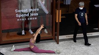 A man wearing a mask to curb the spread of the coronavirus walks past a woman doing a yoga pose for photos in Beijing on Thursday, July 2, 2020