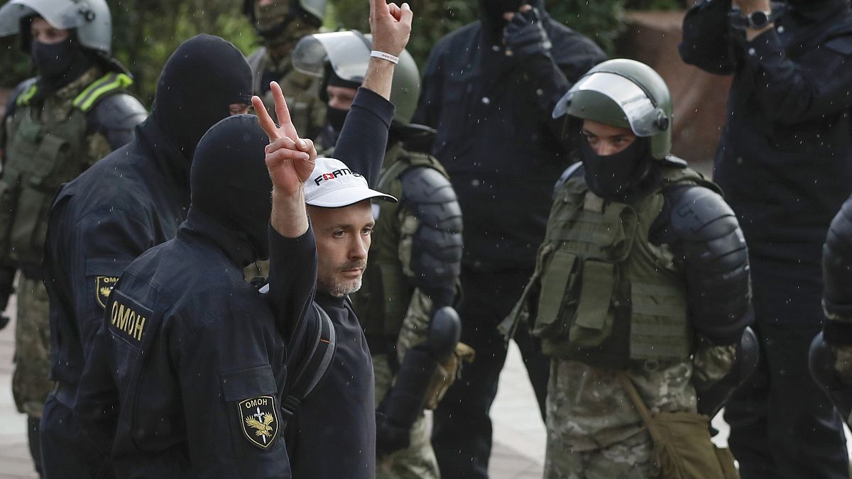 A man makes v-signs in front of a riot police blockade as he is detained during a protest at the Independence Square in Minsk, Belarus, Thursday, Aug. 27, 2020.