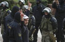 A man makes v-signs in front of a riot police blockade as he is detained during a protest at the Independence Square in Minsk, Belarus, Thursday, Aug. 27, 2020.