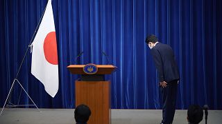 Şinzo Abe, konferans öncesinde Japon bayrağı önünde eğiliyor