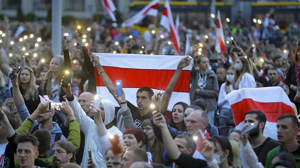 Belarusian opposition supporters with old Belarusian national flags light their smartphones as they gather at Independence Square in Minsk, Belarus, Tuesday, Aug. 25, 2020 Belarusian opposition supporters with old Belarusian national flags light their smartphones as they gather at Independence Square in Minsk, Belarus, Tuesday, Aug. 25, 2020