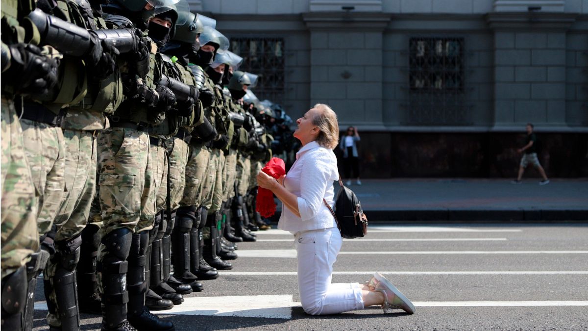 A woman kneels in front of a riot police line as they block Belarusian opposition supporters rally in the center of Minsk, Belarus, Sunday, Aug. 30, 2020
