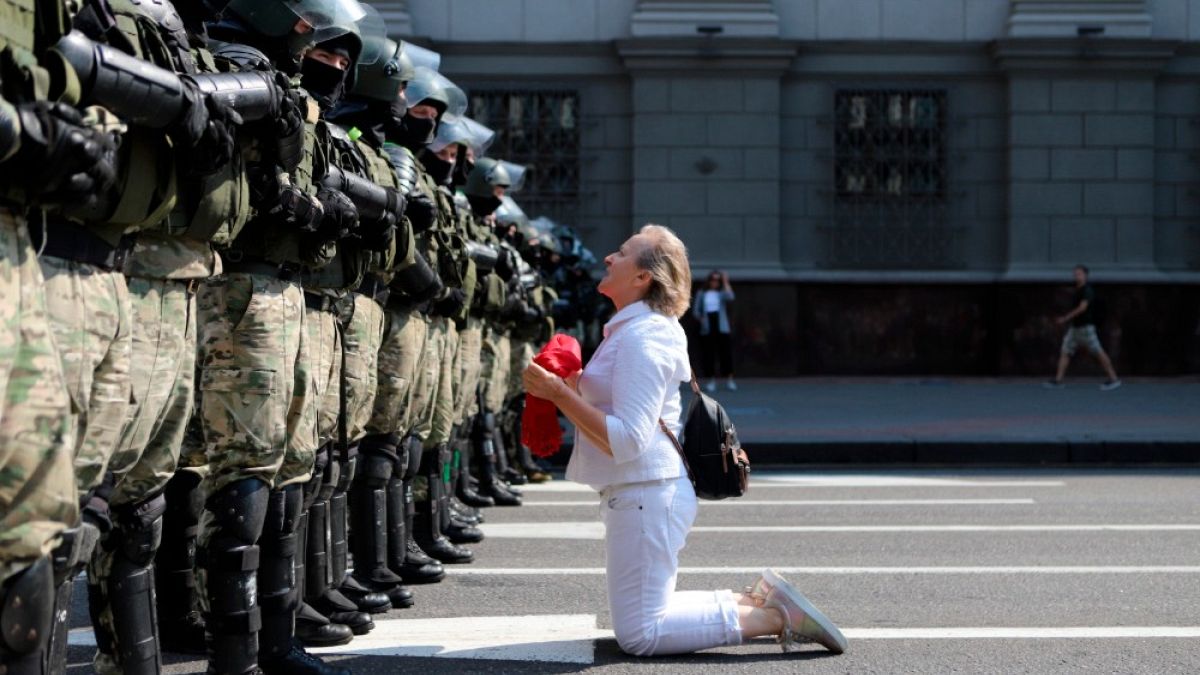 Una donna si inginocchia davanti agli agenti della polizia antisommossa, che blocca la manifestazione dei sostenitori dell'opposizione bielorussa, Minsk