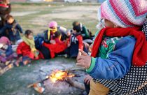 A small child is held by a fire as migrants pause on their way to Greece near Doyran, Turkey, Sunday, March. 1, 2020.