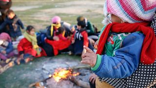 A small child is held by a fire as migrants pause on their way to Greece near Doyran, Turkey, Sunday, March. 1, 2020.