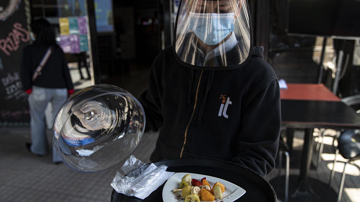 Un camarero con mascarilla y visera de protección sirve un plato en Santiago de Chile